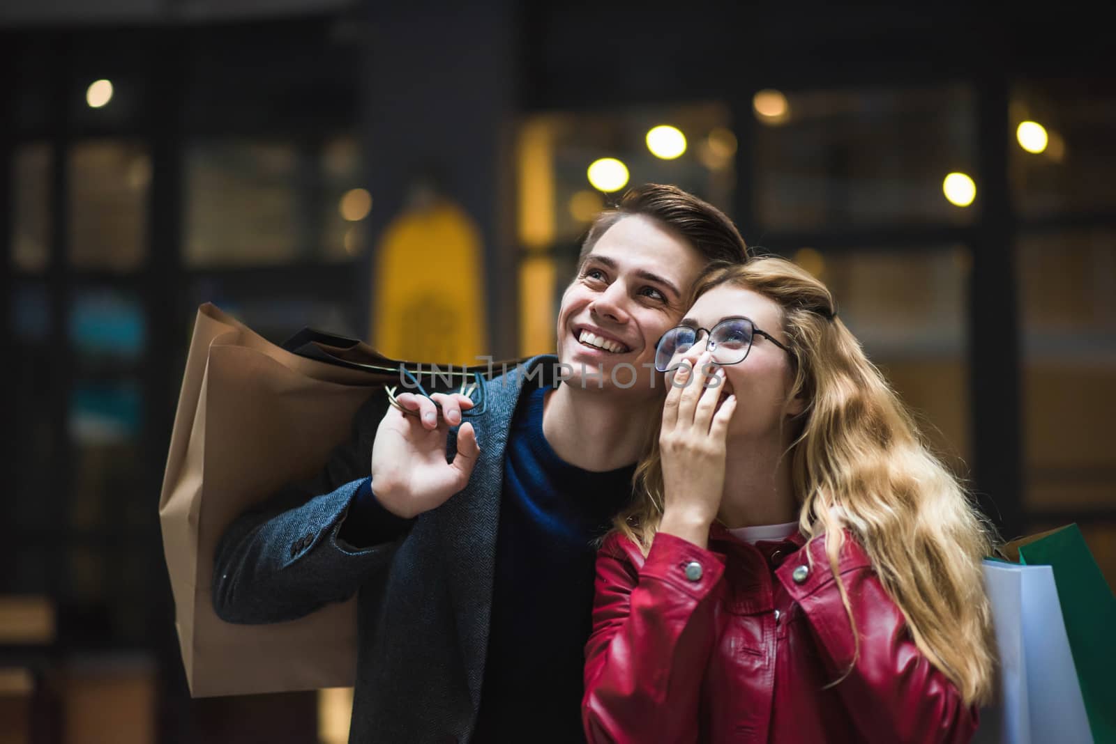 Beautiful couple with shopping bags is talking and smiling while doing shopping in the mall focus on the surprised woman.