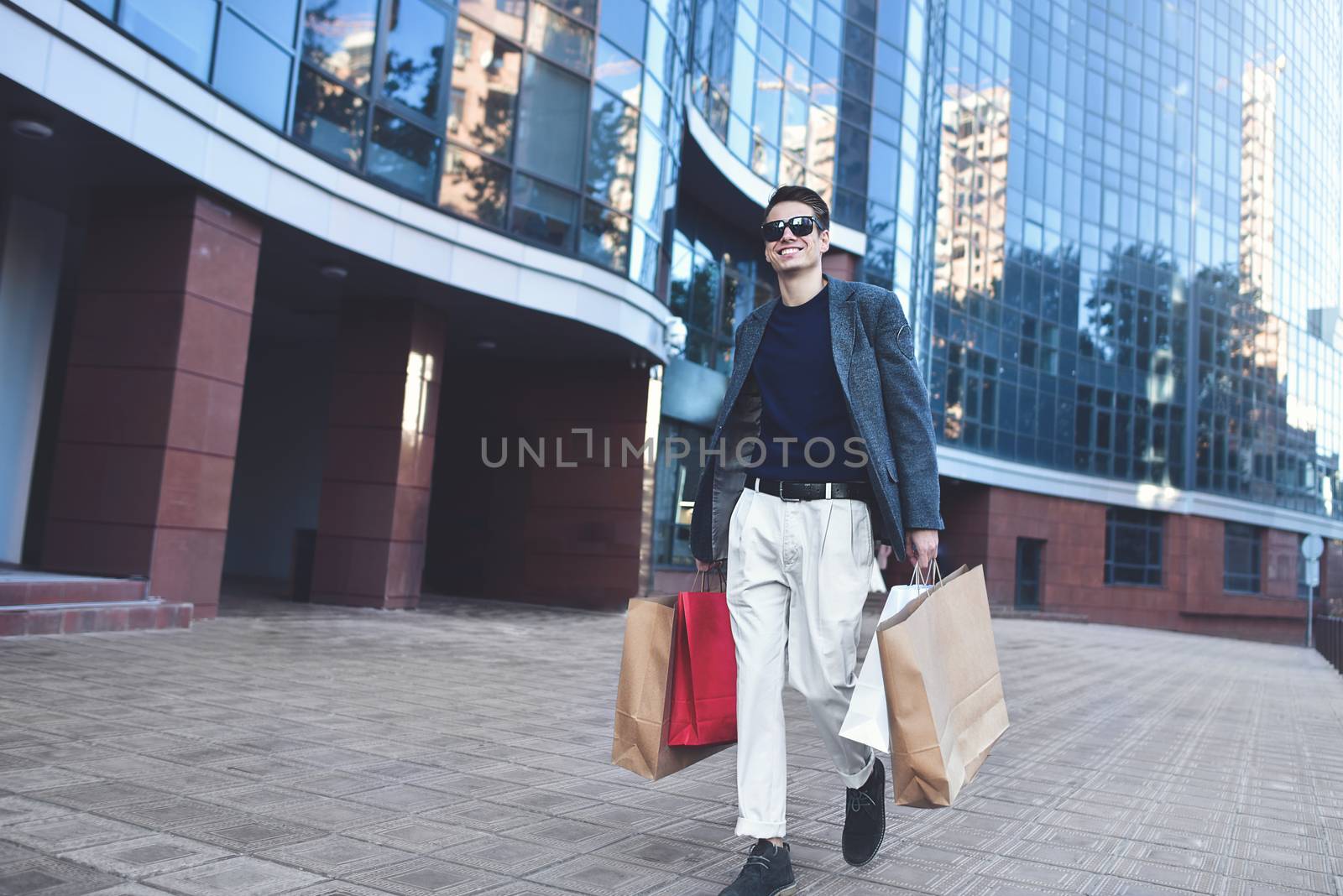 Happy stylish young man walking in urban street and enjoying Black Friday shopping in trendy stores in city. by Nickstock