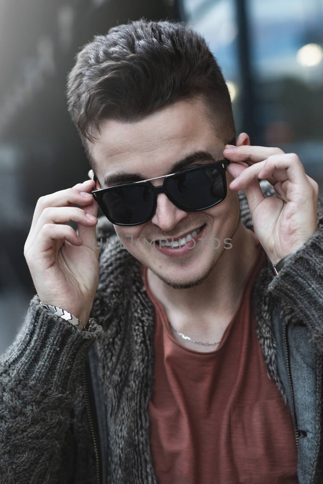 Closeup of cheerful young caucasian man in sunglasses standing and smiling over street background
