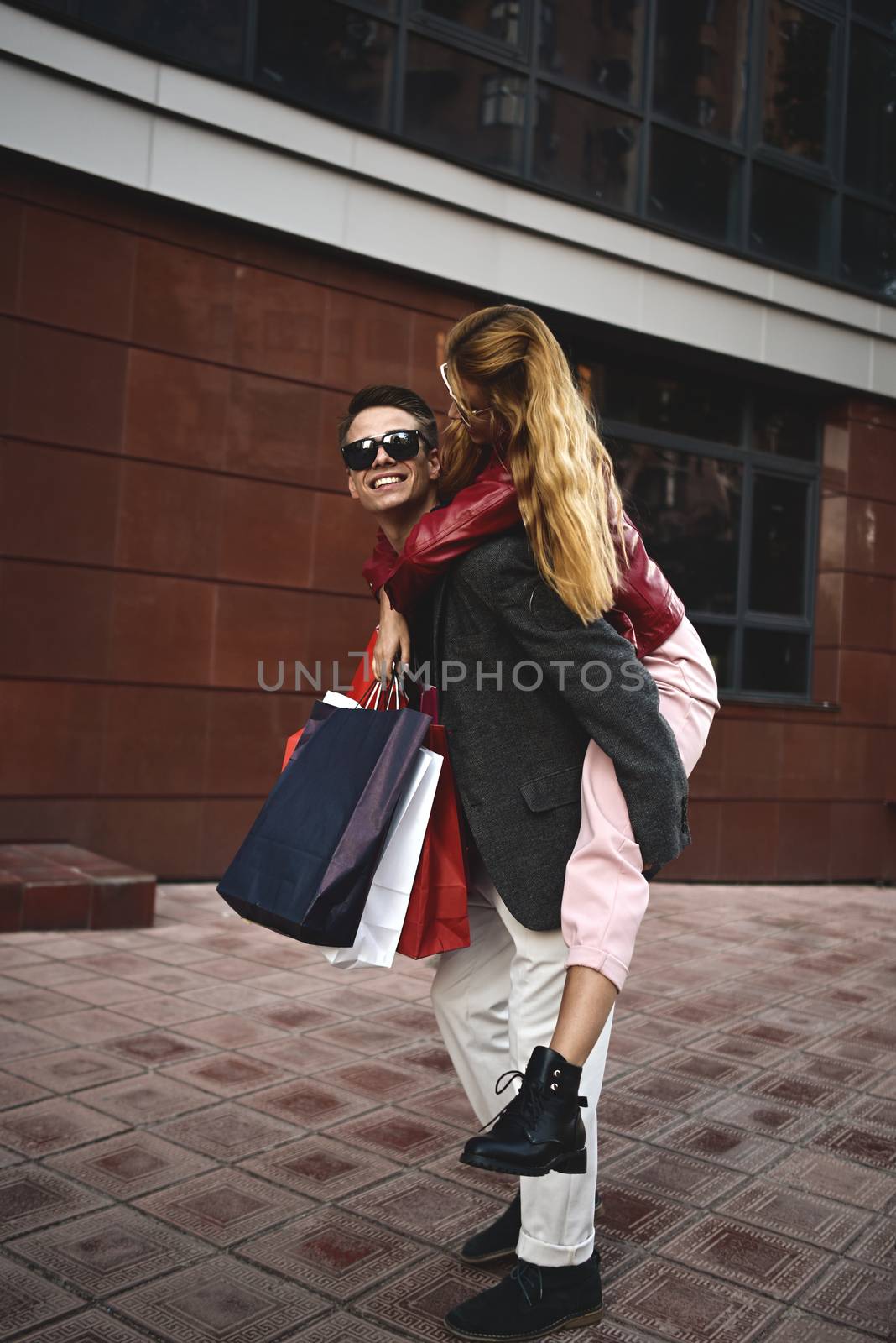 Couple in shopping together. Happy couple shopping together and having fun. Boyfriend carrying his girlfriend on the piggyback. by Nickstock