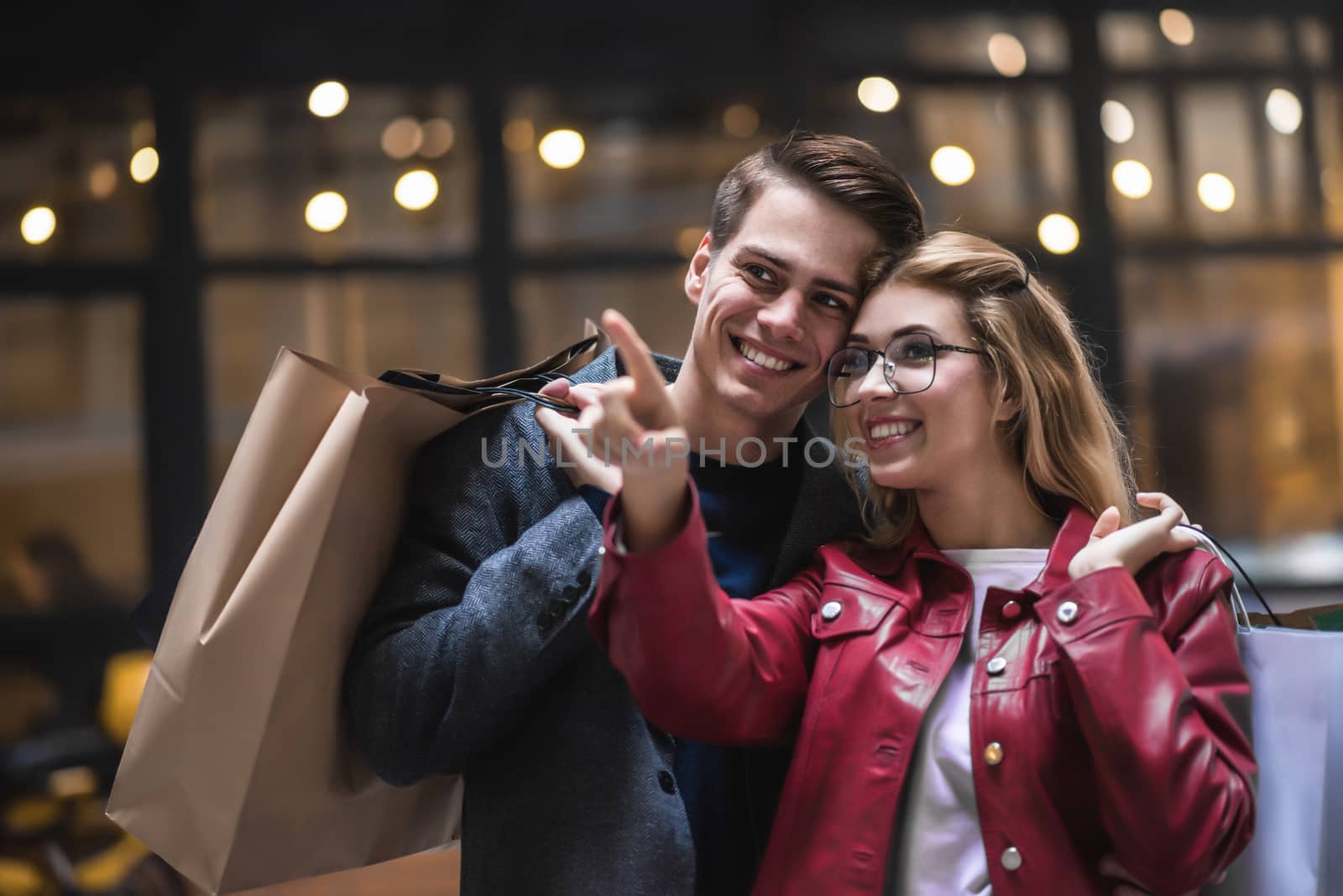 Beautiful couple with shopping bags is talking and smiling while doing shopping in the mall focus on the woman