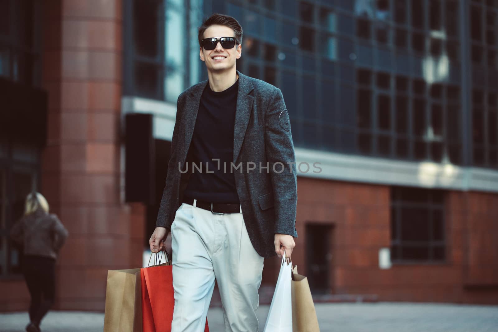 Serious cool guy with sunglasses and paper bags walking at street.
