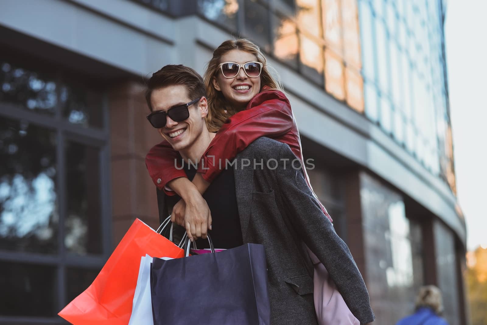 Happy couple shopping together and having fun. Boyfriend carrying his girlfriend on the piggyback.
