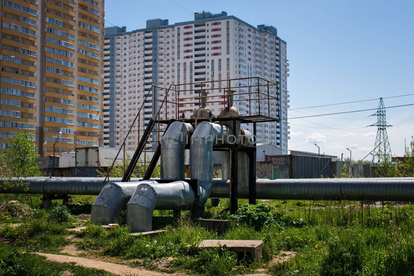 Large diameter pipes with hot and cold water installed above the ground near residential buildings in summer in sunny weather