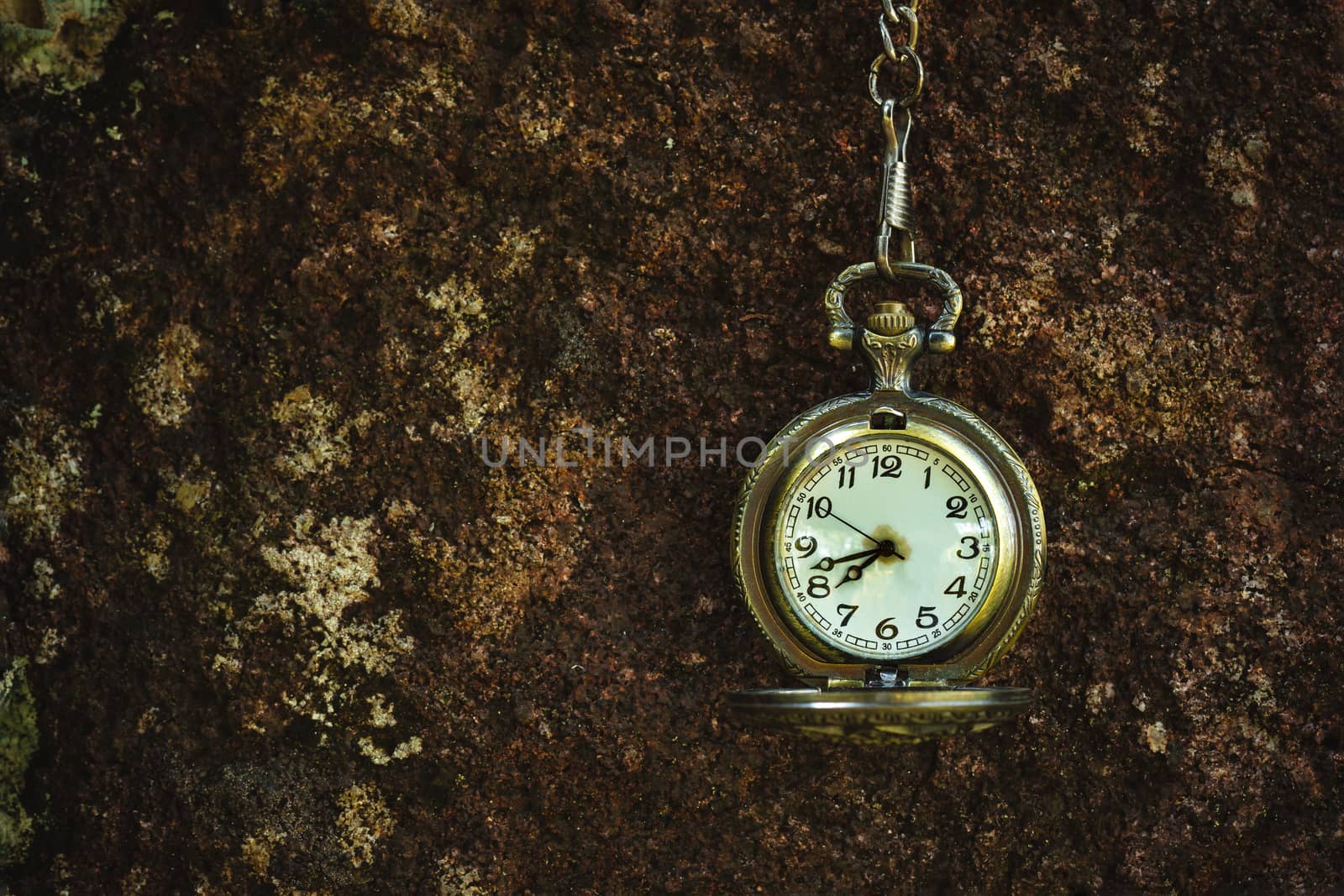 Vintage old pocket watch hanged on the rock background. by SaitanSainam