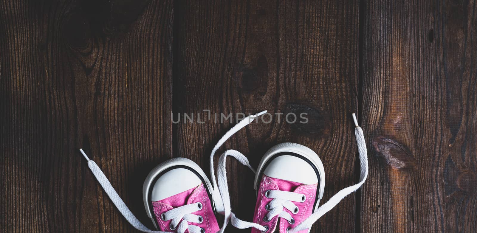 small pink textile sneakers on a brown wooden background by ndanko