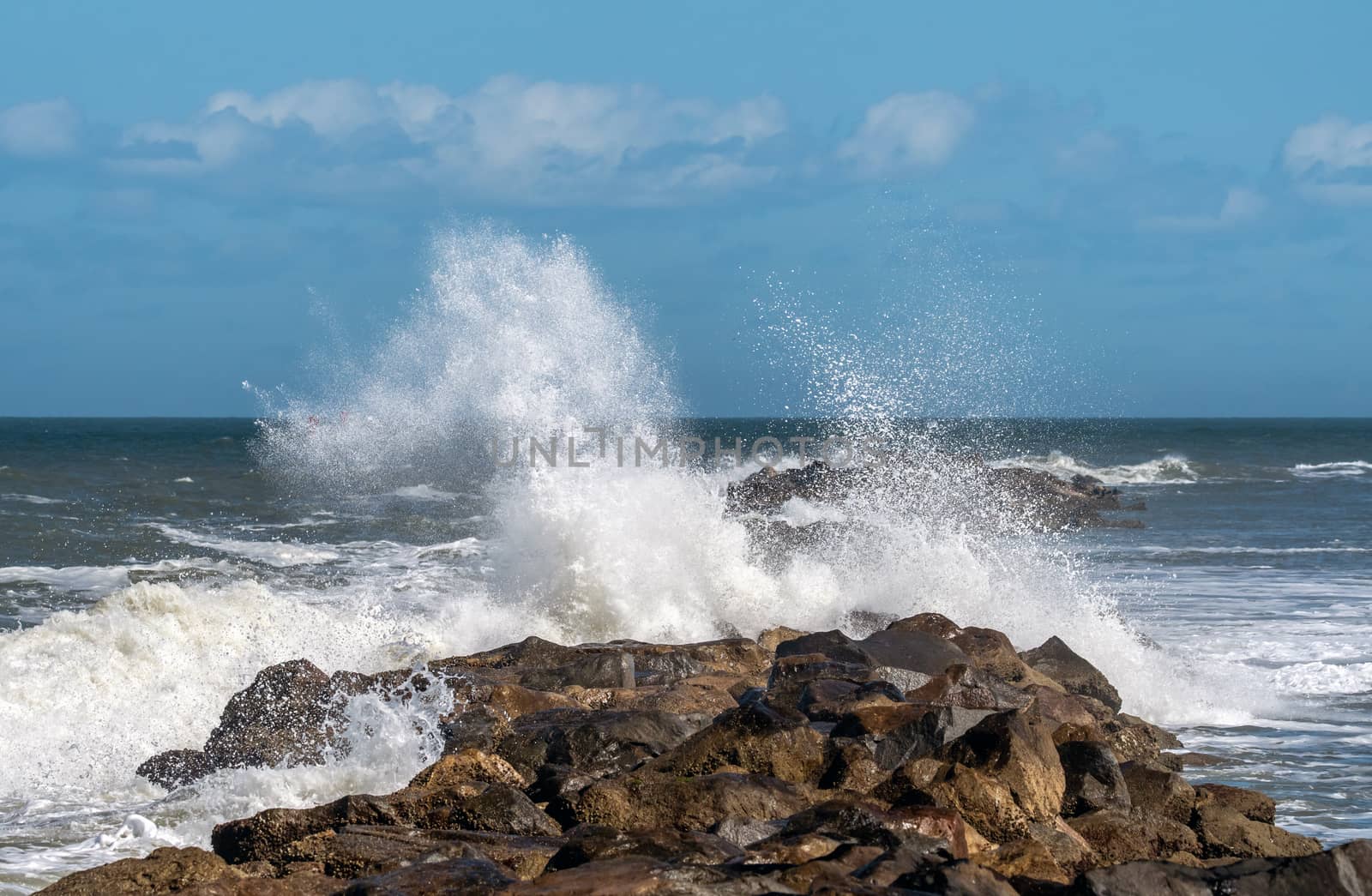 Waves breaking over a rock jetty wall.