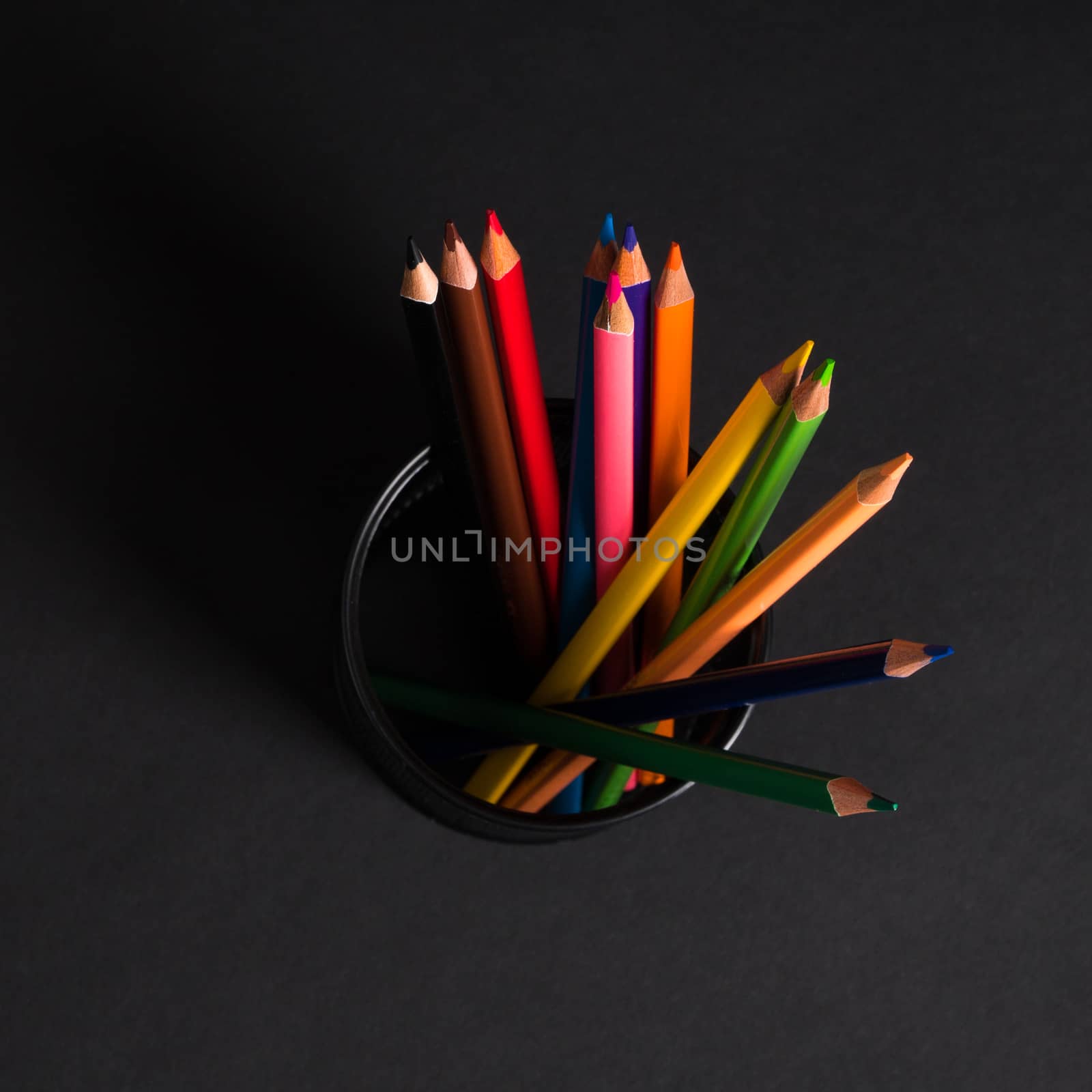 set of colored pencils in a basket on a black background, isolated. back to school