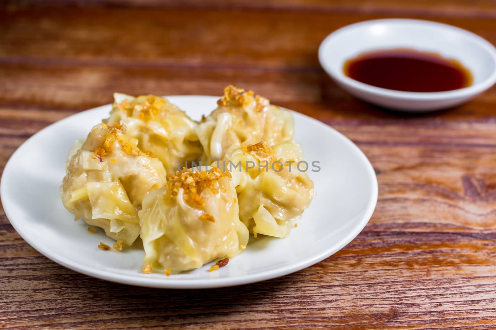 Chinese Steamed Dumpling, Shumai on white dish served with soy sauce on wooden table. Delicious Dimsum pork.