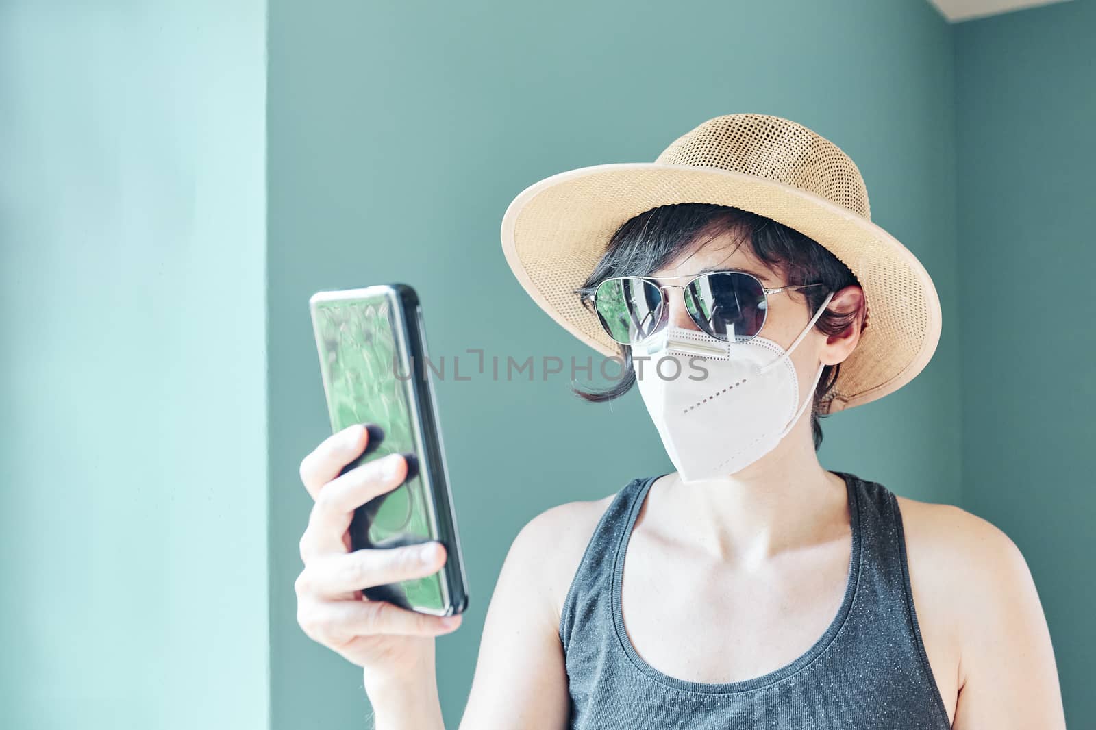 Woman with straw hat and face mask using mobile phone at Covid time