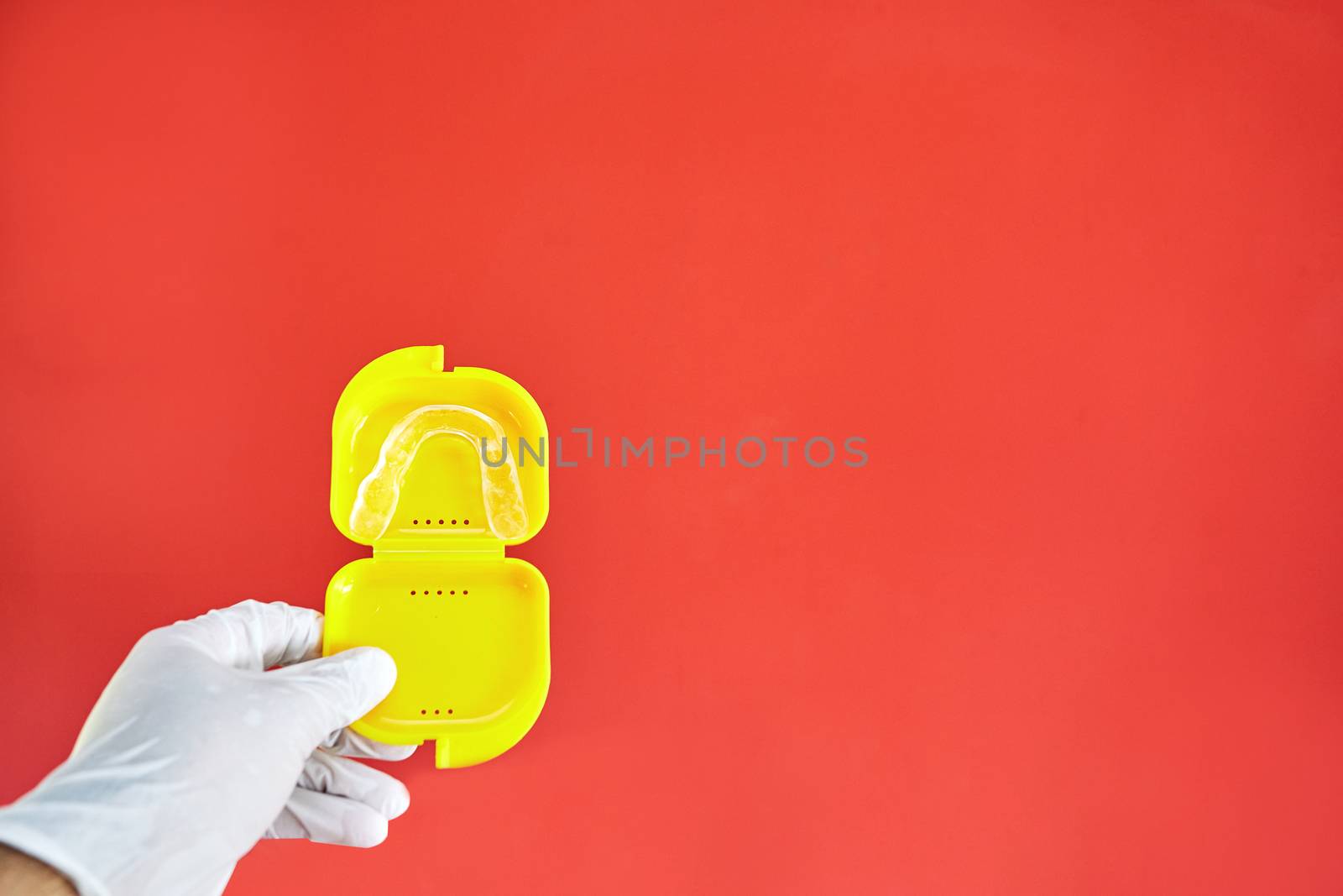 Invisible bracelets in a yellow case on a red background held in one hand by a latex glove