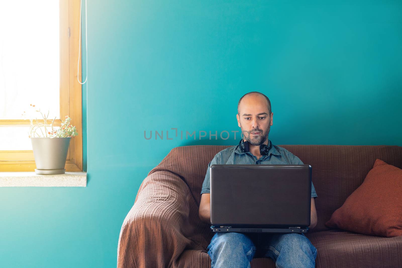 Man sitting on a sofa working from home with his laptop and headphones