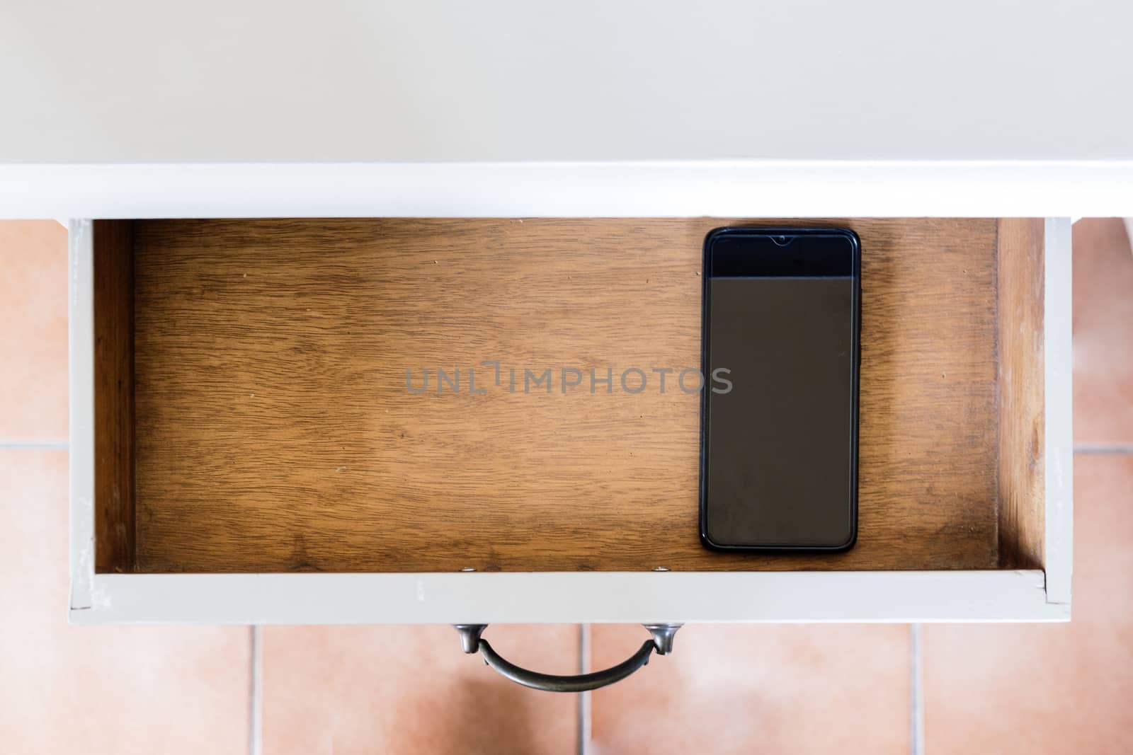 Mobile phone stored on a bedside table in a drawer that is open