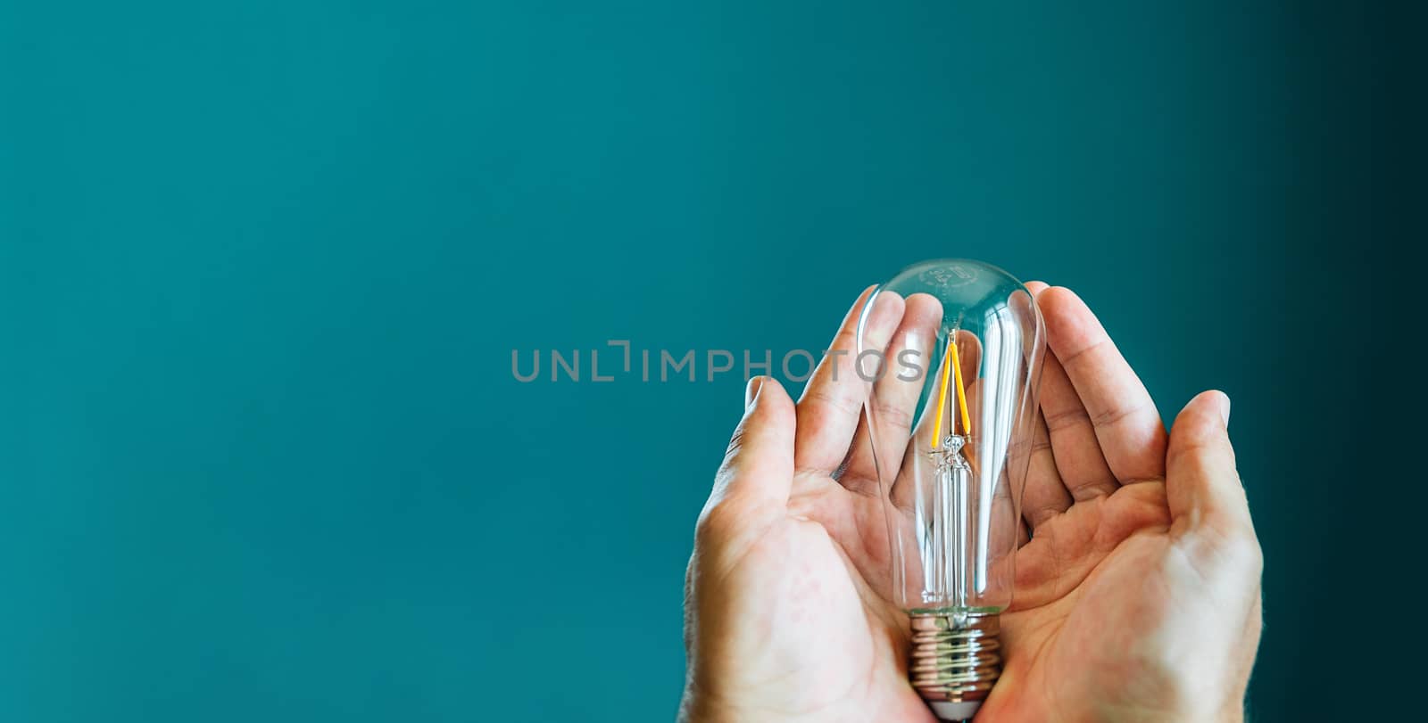 Two hands holding a light bulb on a green background with copy space