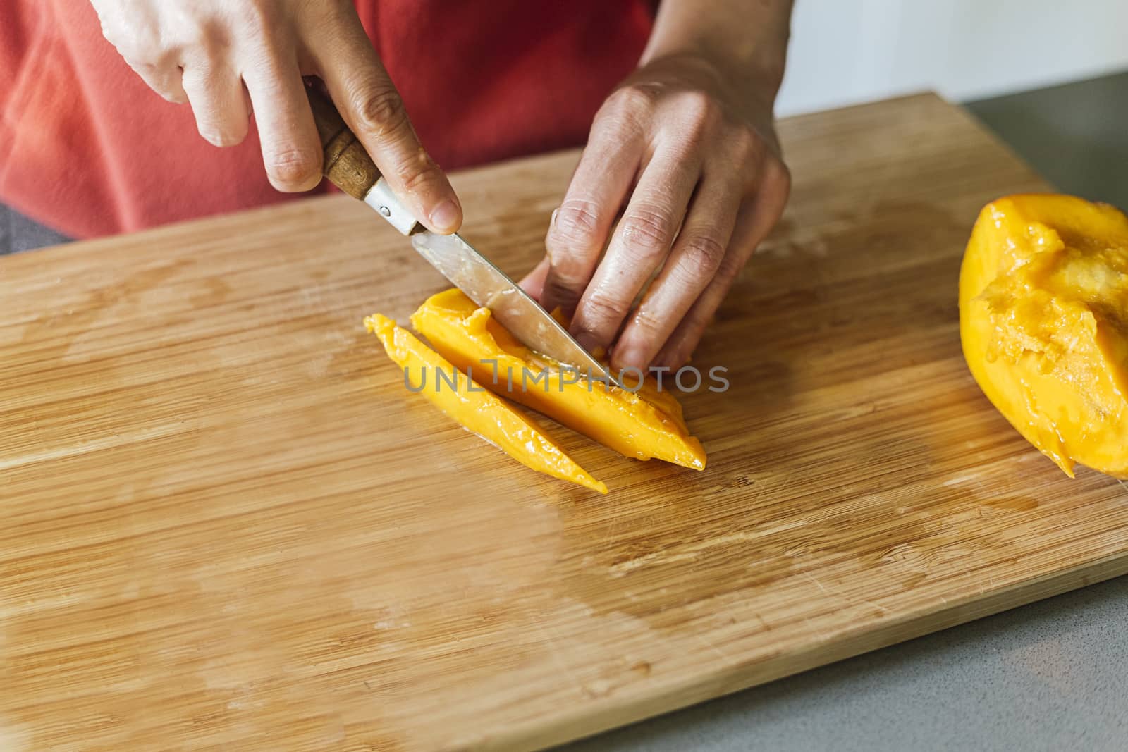 Woman cutting mango on a wooden board to prepare a healthy salad by Daniel_Mato