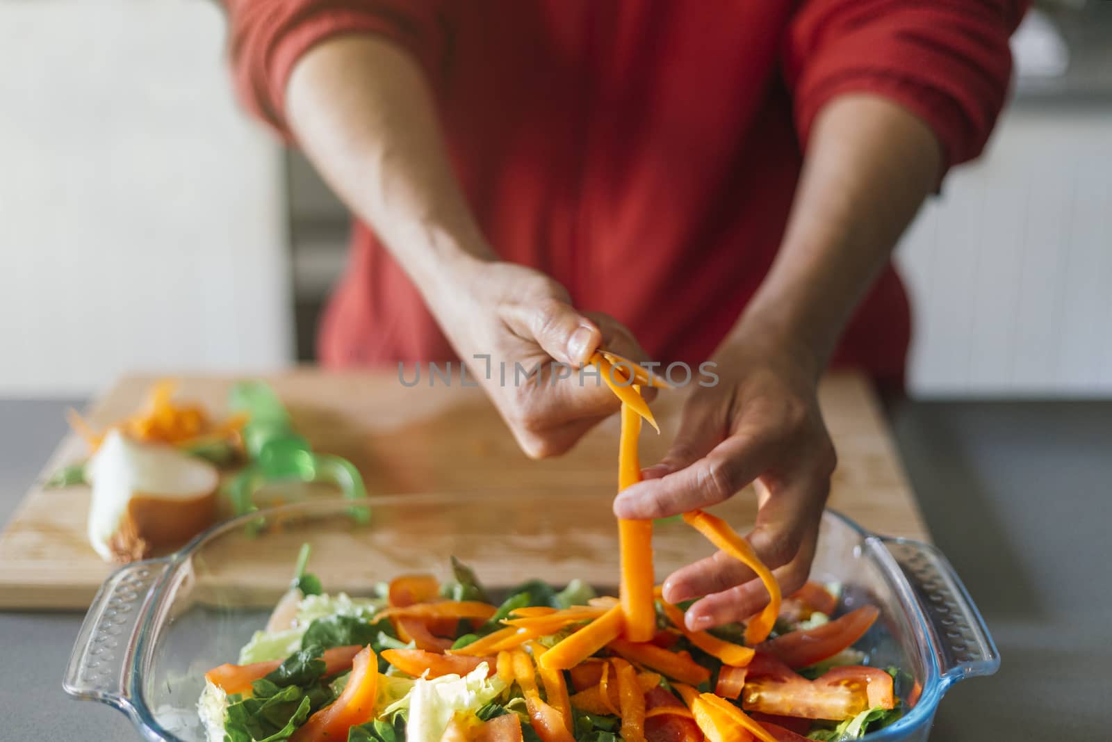 Woman cutting carrots and putting them in a salad with her hands