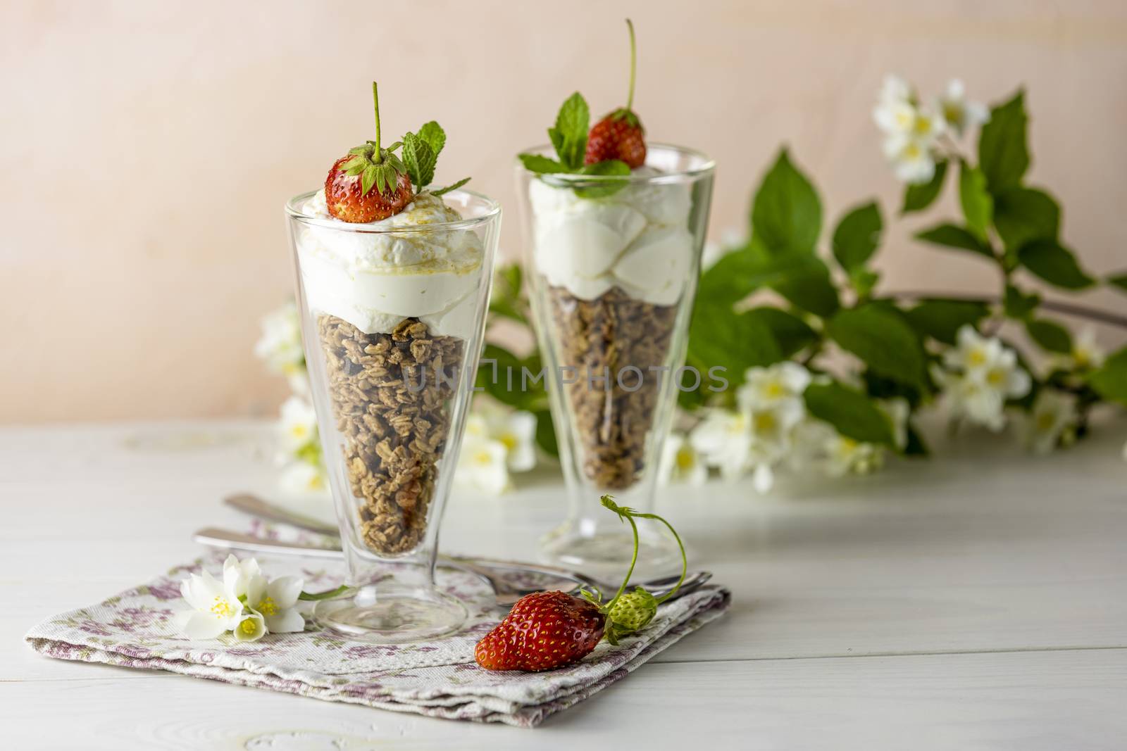 Two glass of healthy breakfast with granola and greek yogurt decorated by mint and raw strawberry served on white wooden background.