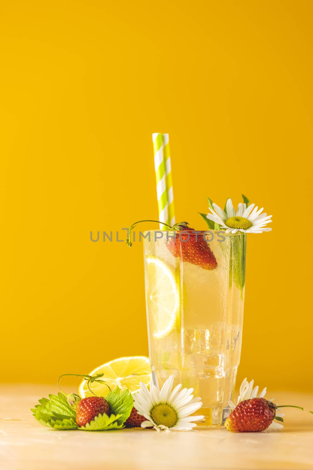 Glasses of cold icy refreshing drink with lemon and strawberry. Bright yellow background.  Fresh cocktail drinks with ice fruit, herb and chamomile decoration.