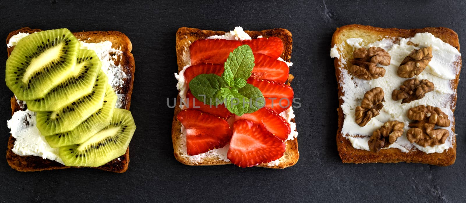 three toasts with mild cottage cheese, strawberries, kiwi and nuts on a black background, top view