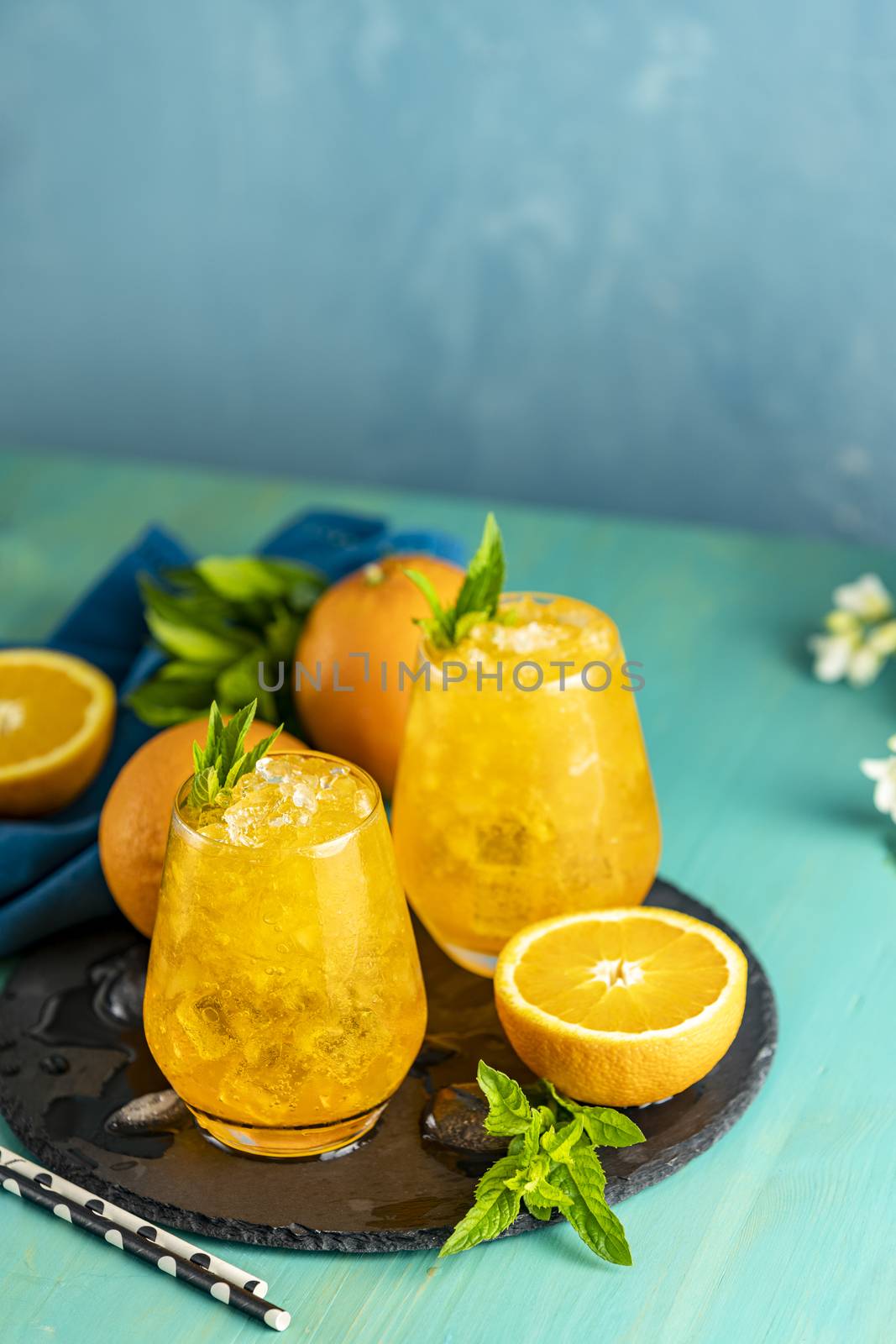 Orange drink with ice. Two glass of orange ice drink with fresh mint on wooden turquoise table surface. Alcoholic nonalcoholic summer fresh drink beverage