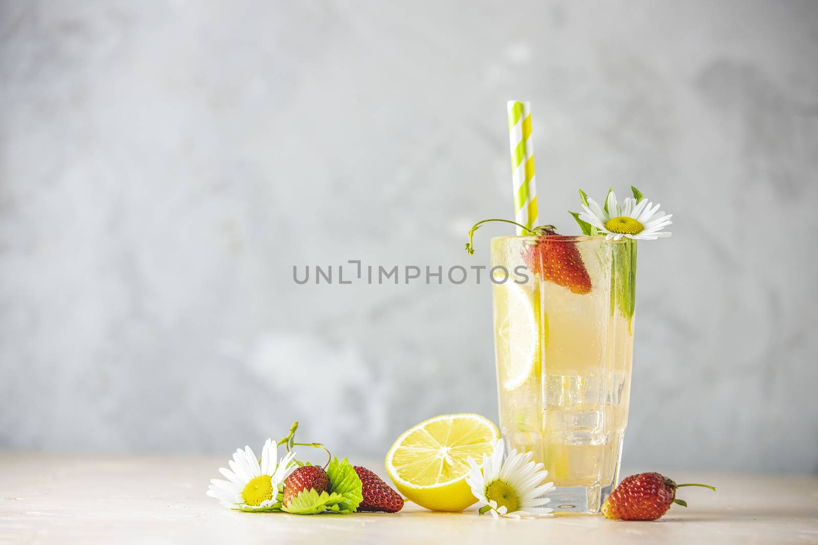 Glasses of cold icy refreshing drink with lemon and strawberry served on light pink table.  Fresh cocktail drinks with ice fruit, herb and chamomile decoration.