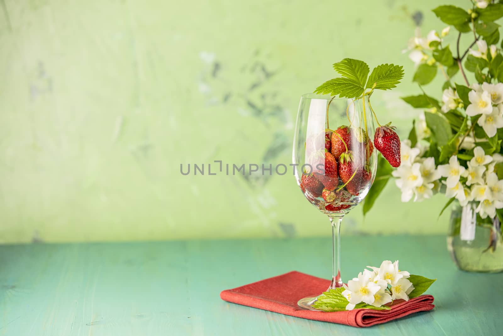 Fresh ripe raw strawberry with green leaves in the wine glass on green surface with red napkin.