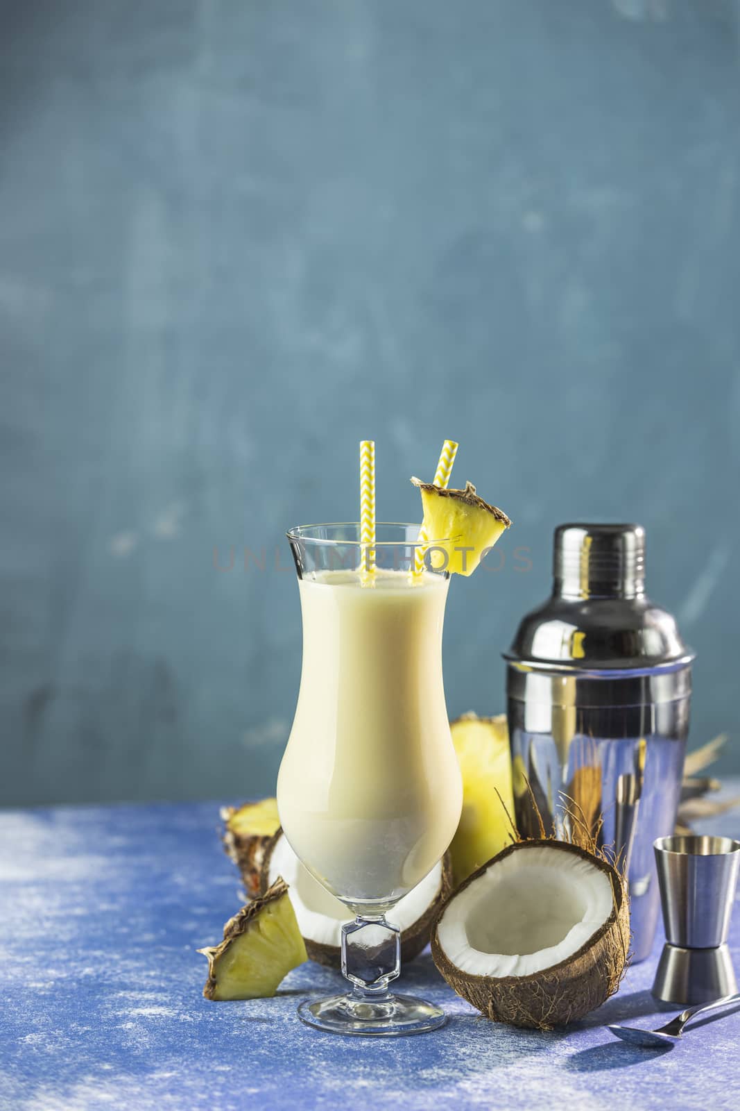 Glass of tasty Frozen Pina Colada Traditional Caribbean cocktail decorated by slice of pineapple, served with bar tools on blue concrete background