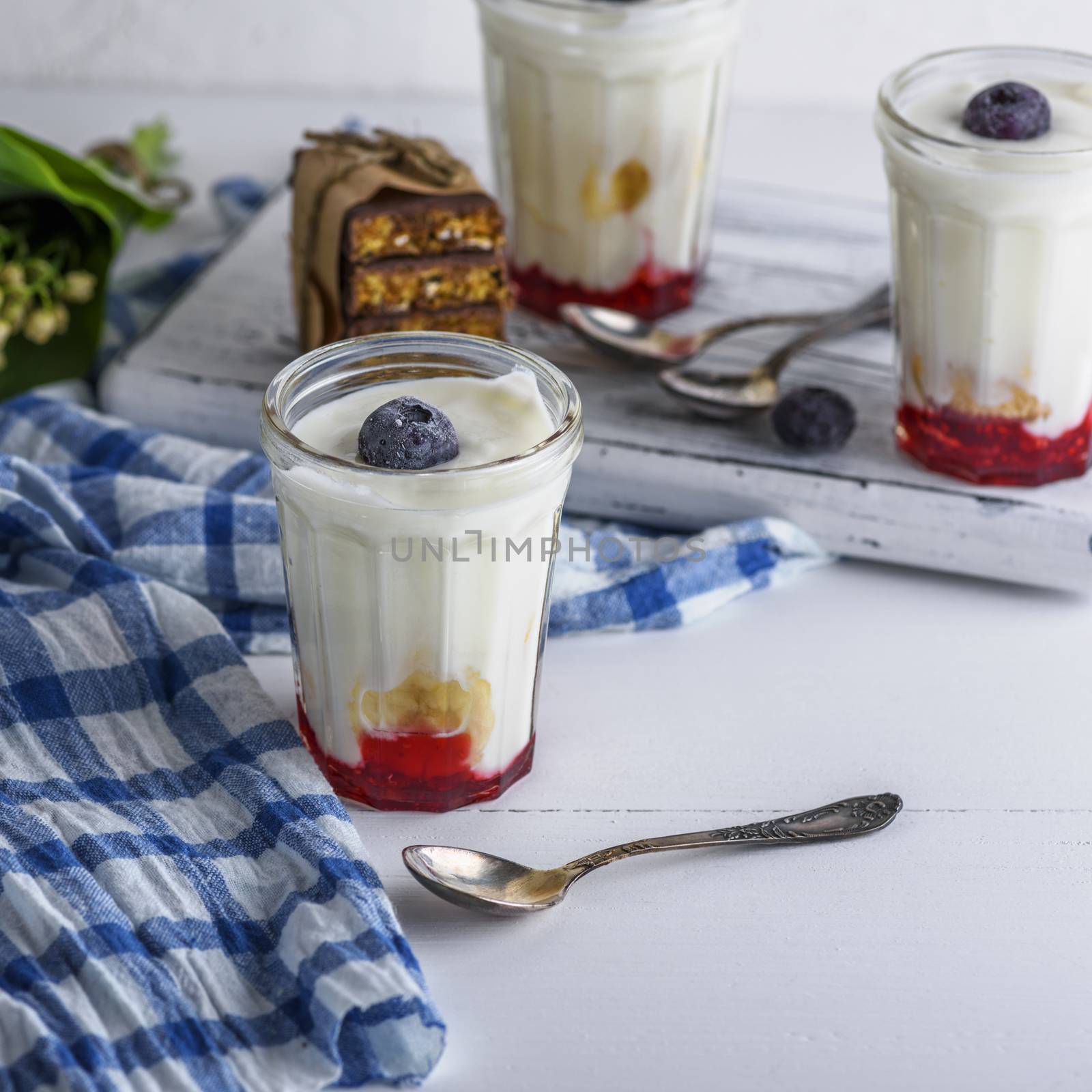 homemade yogurt in transparent glass with syrup and banana on a white wooden background, top view