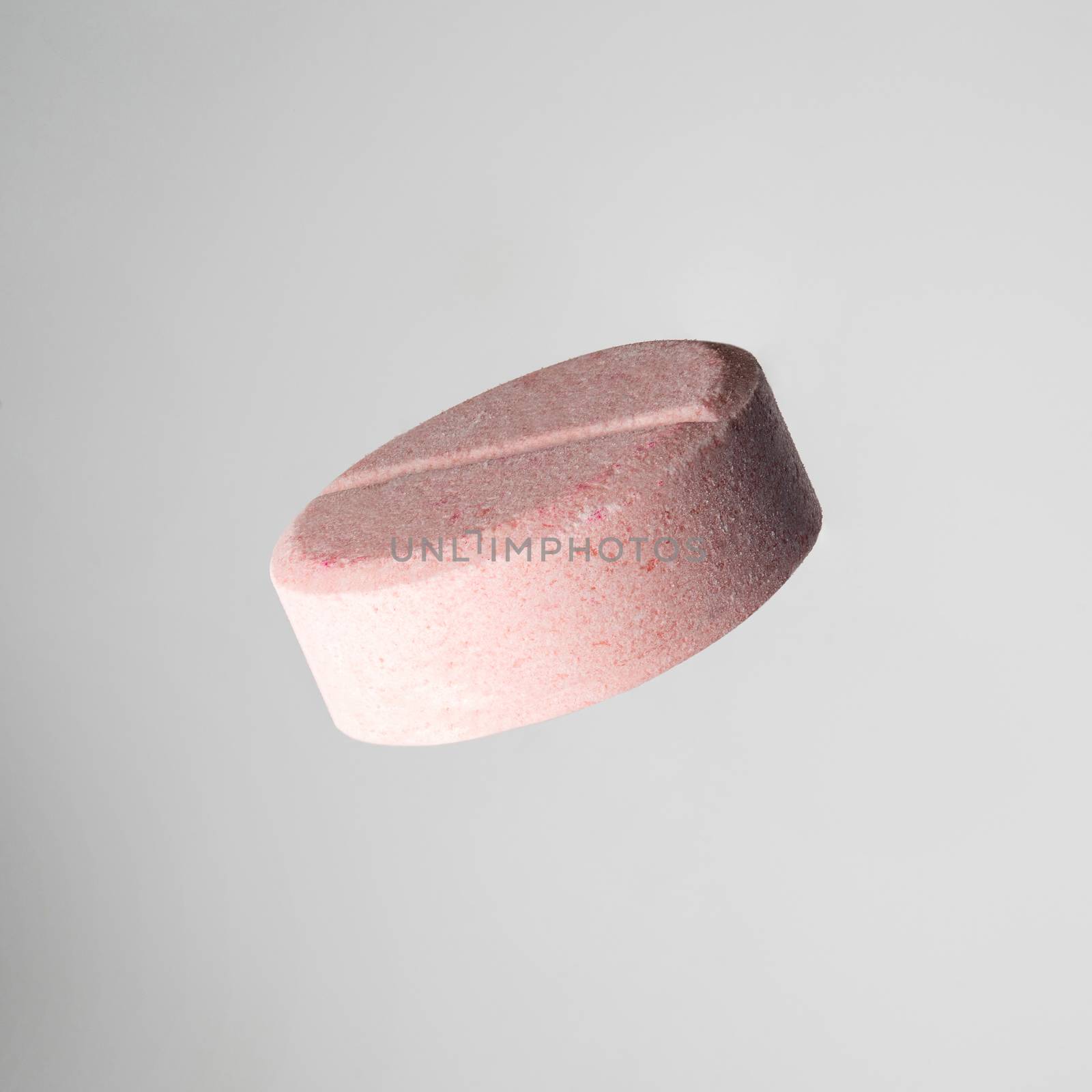 one pink medical ascorbic pill on light grey background. Isolated, close-up
