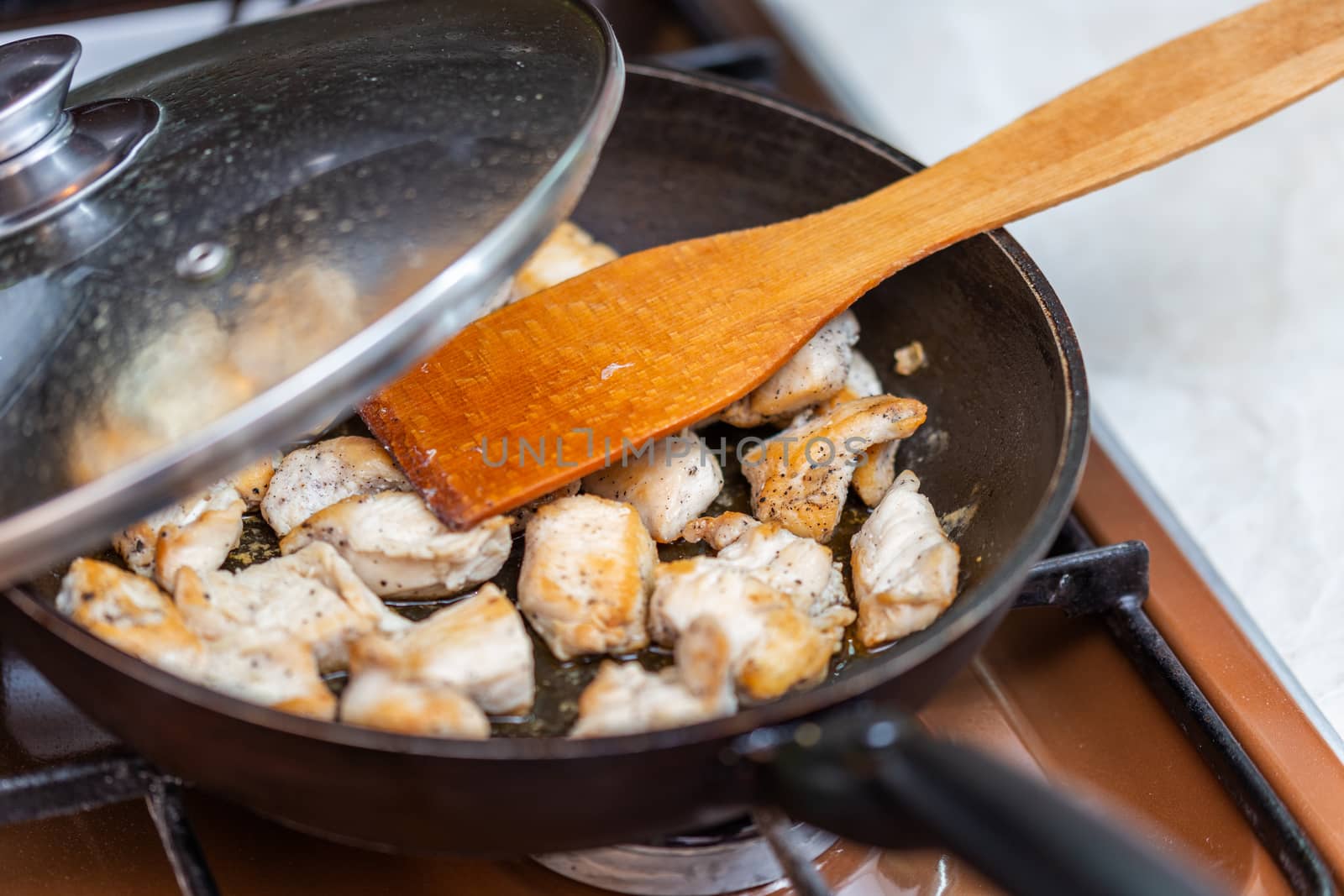 fried chicken in a open pan with ground black pepper and wooden kitchen spatula, closeup with selective focus