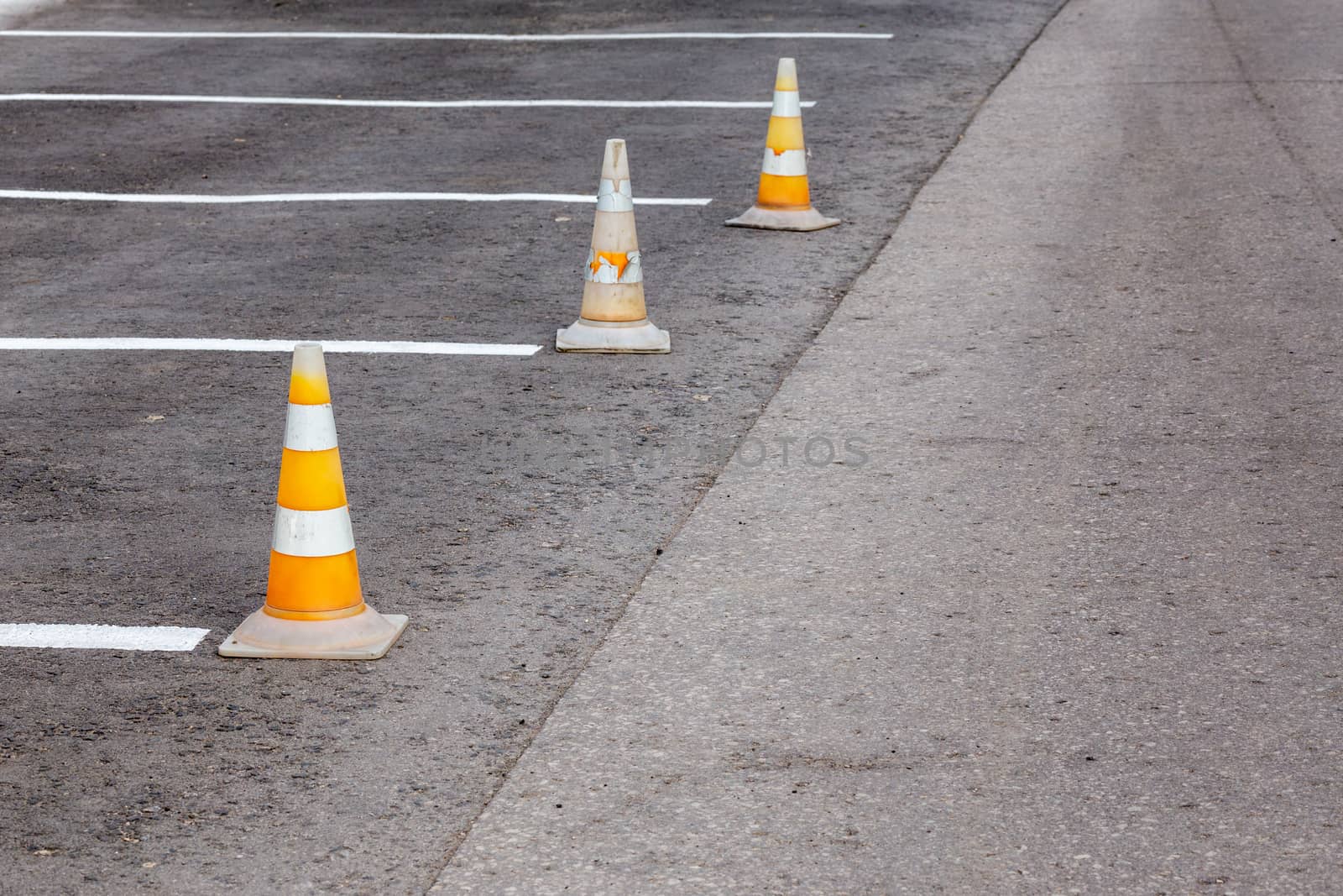 Orange road cones on a asphelt driving area with white lines, close-up with selective focus and backgropund blur.