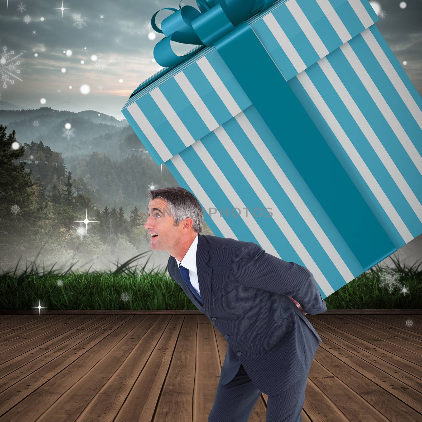 Stylish man with giant gift against mountain range beyond wooden floor