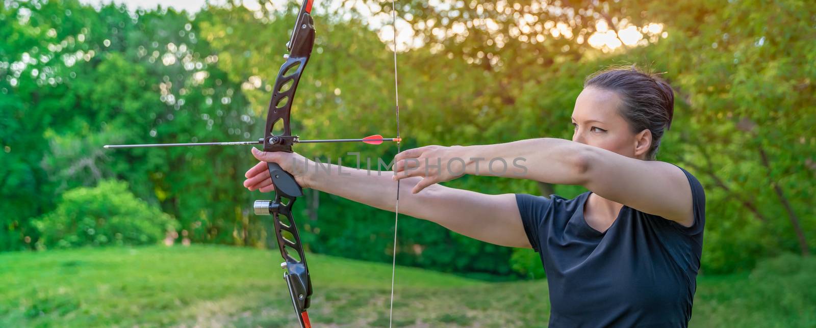archery in nature, young woman aiming an arrow at a target by Edophoto