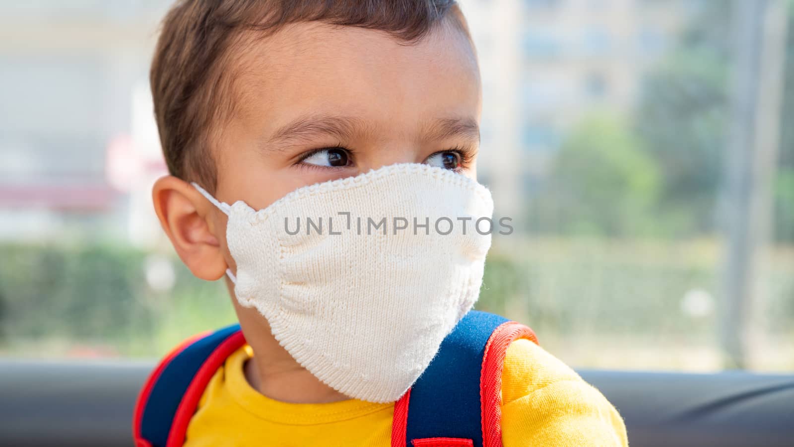 Little boy wearing white knitted cotton face mask as a protection against the novel coronavirus and Covid-19 disease.