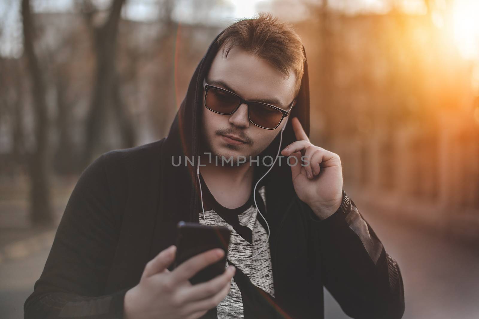 Man in Hood with headphones looking at smartphone.