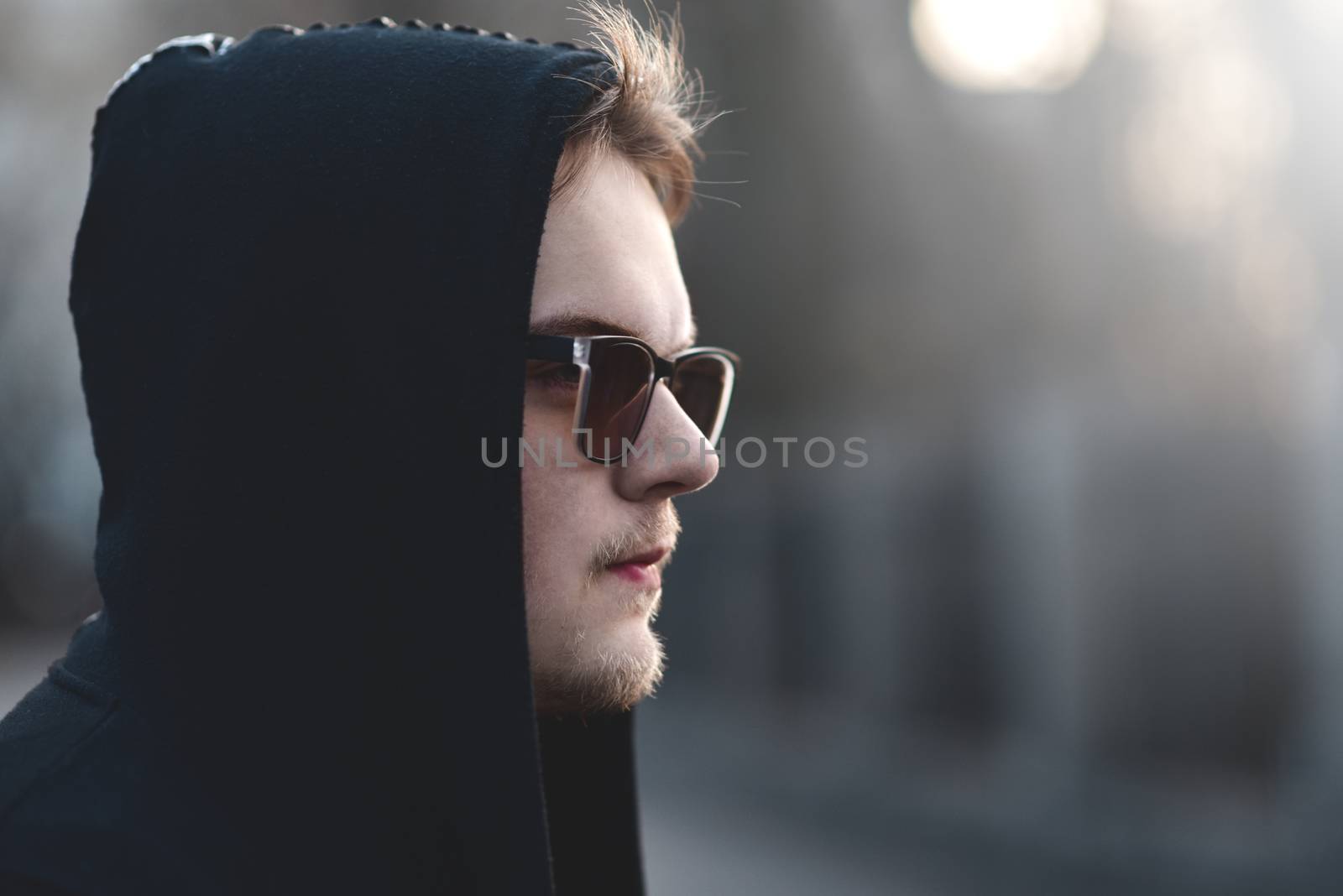 Portrait of fashion man in a black sweater with a hood and sunglasses