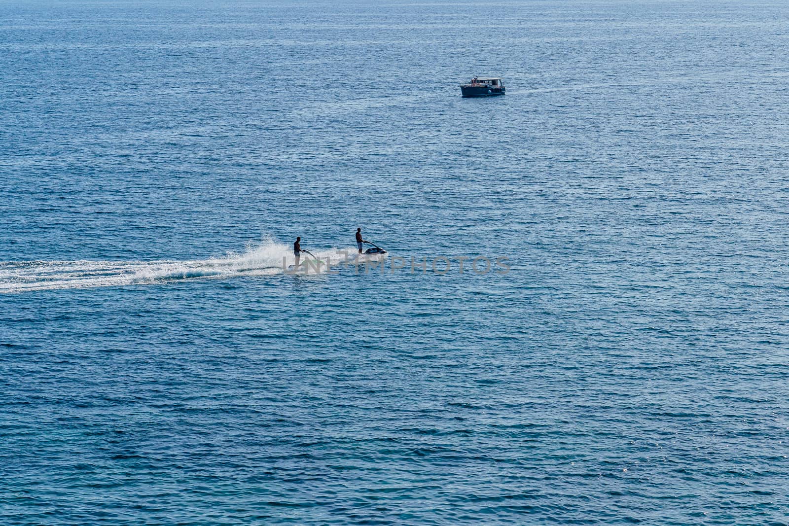 two people ride water bikes in the sea on the background of the boat, summer day