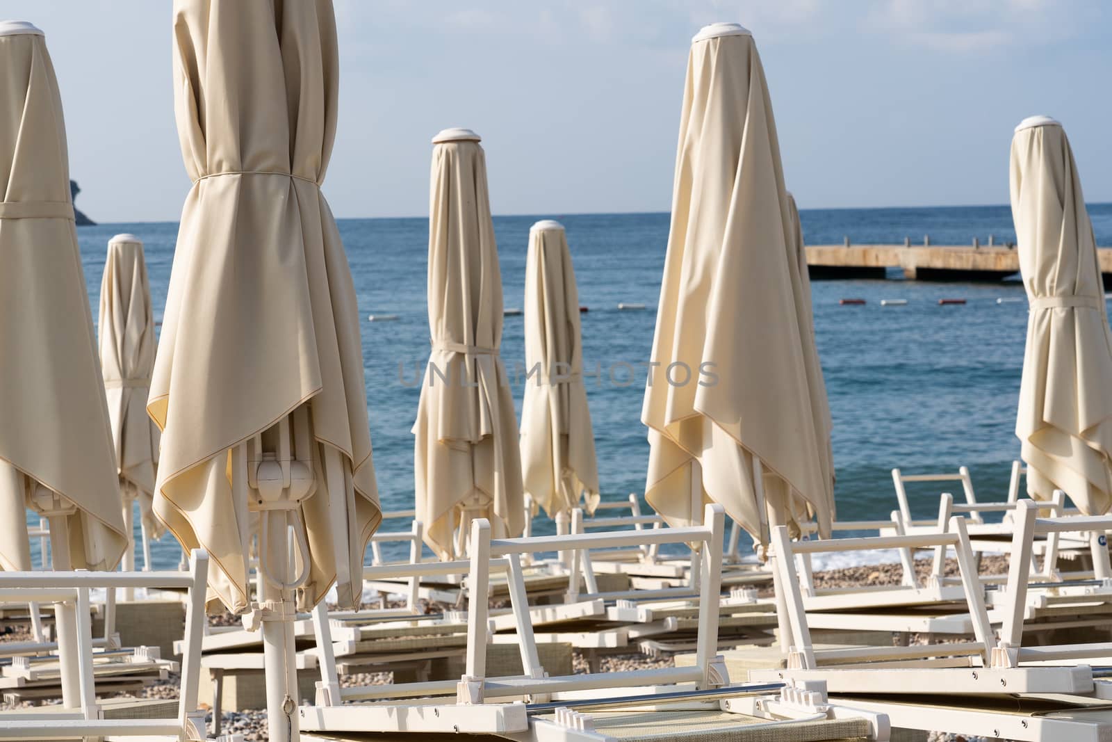 Folded beach umbrellas on the background of the sea. The beach is getting ready to open.