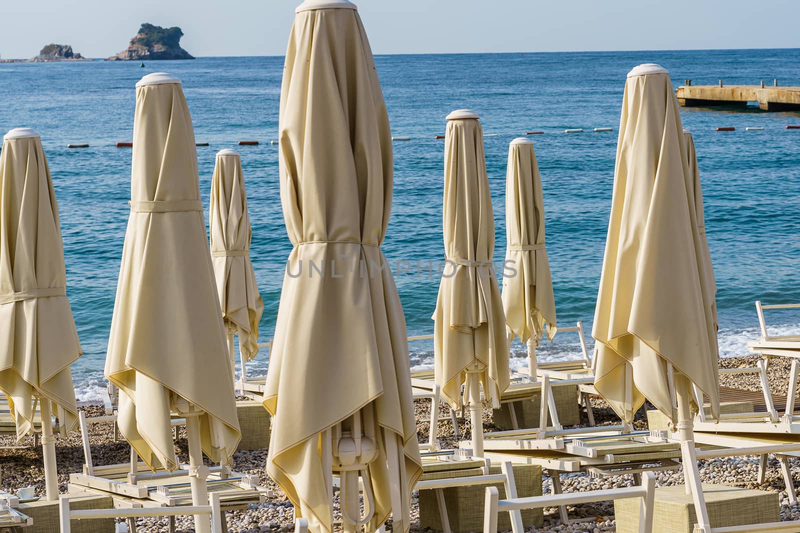 Folded beach umbrellas on the background of the sea. The beach is getting ready to open.