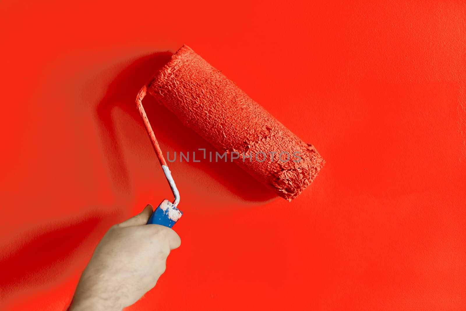 Male hand painting wall with paint roller. Painting apartment, renovating with red color paint