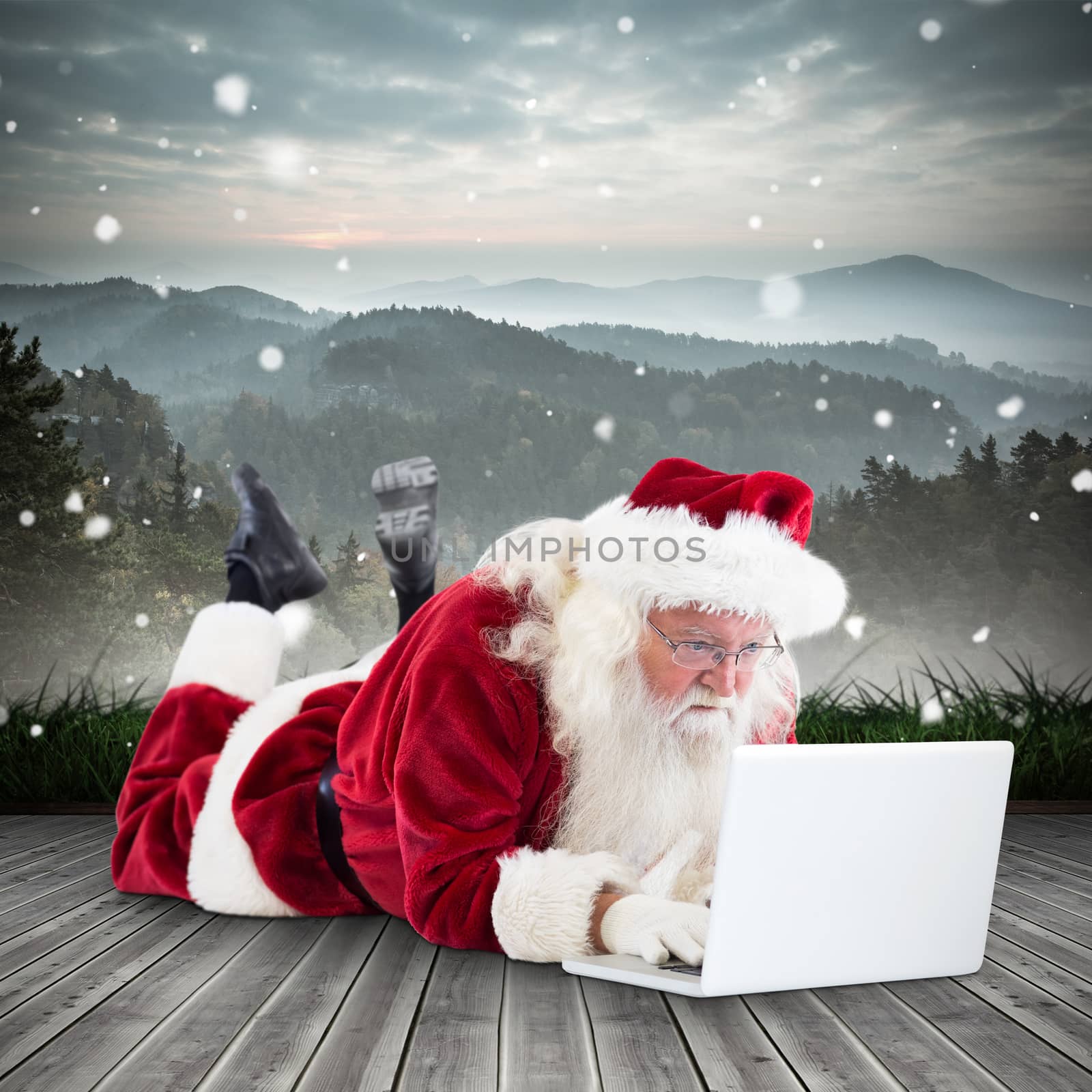 Santa lies in front of his laptop against mountain range beyond wooden floor
