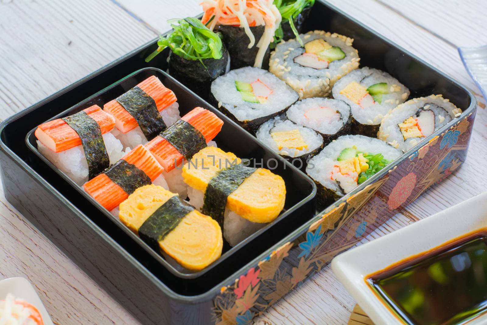 Set of variety sushi, Tamagoyaki, crabsticks sushi and maki in bento box served with soy sauce and wasabi. Delicious japanese food.