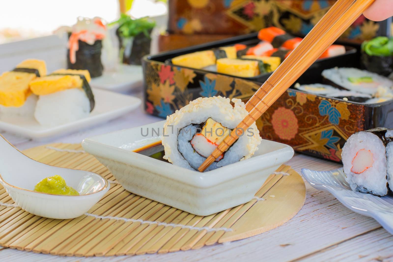 Eatting tamagoyaki maki and white sesame seeds with wooden chopsticks and soy sauce in white bowl. Delicious japanese food.