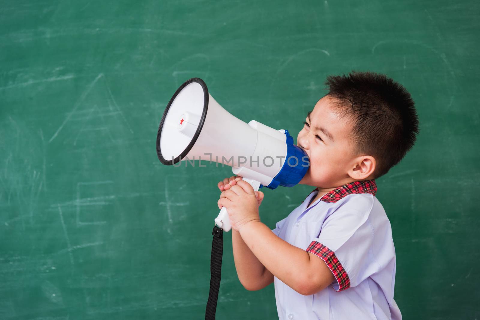 Back to School. Asian funny cute little child boy kindergarten preschool in student uniform speaking through megaphone against on green school blackboard, First time to school education concept