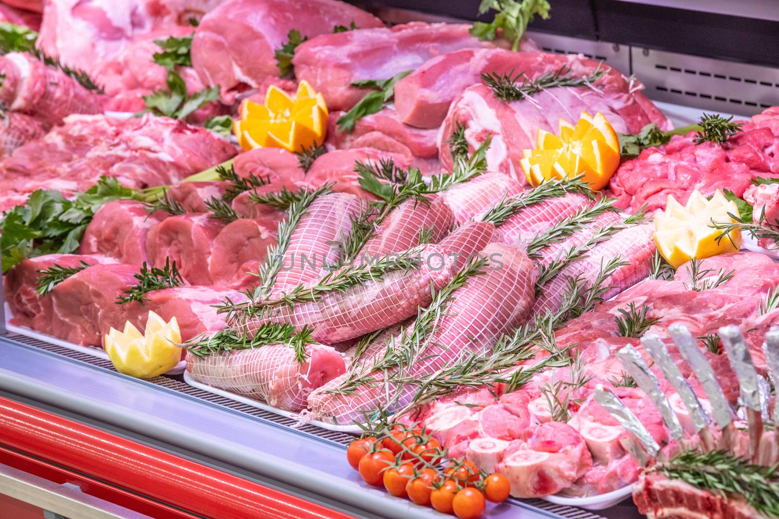 Meat department in butchery inside a mall. Various types of meat displayed in an orderly and creative way. Shelves of a food supermarket. Orange and vegetables for decoration and topping.