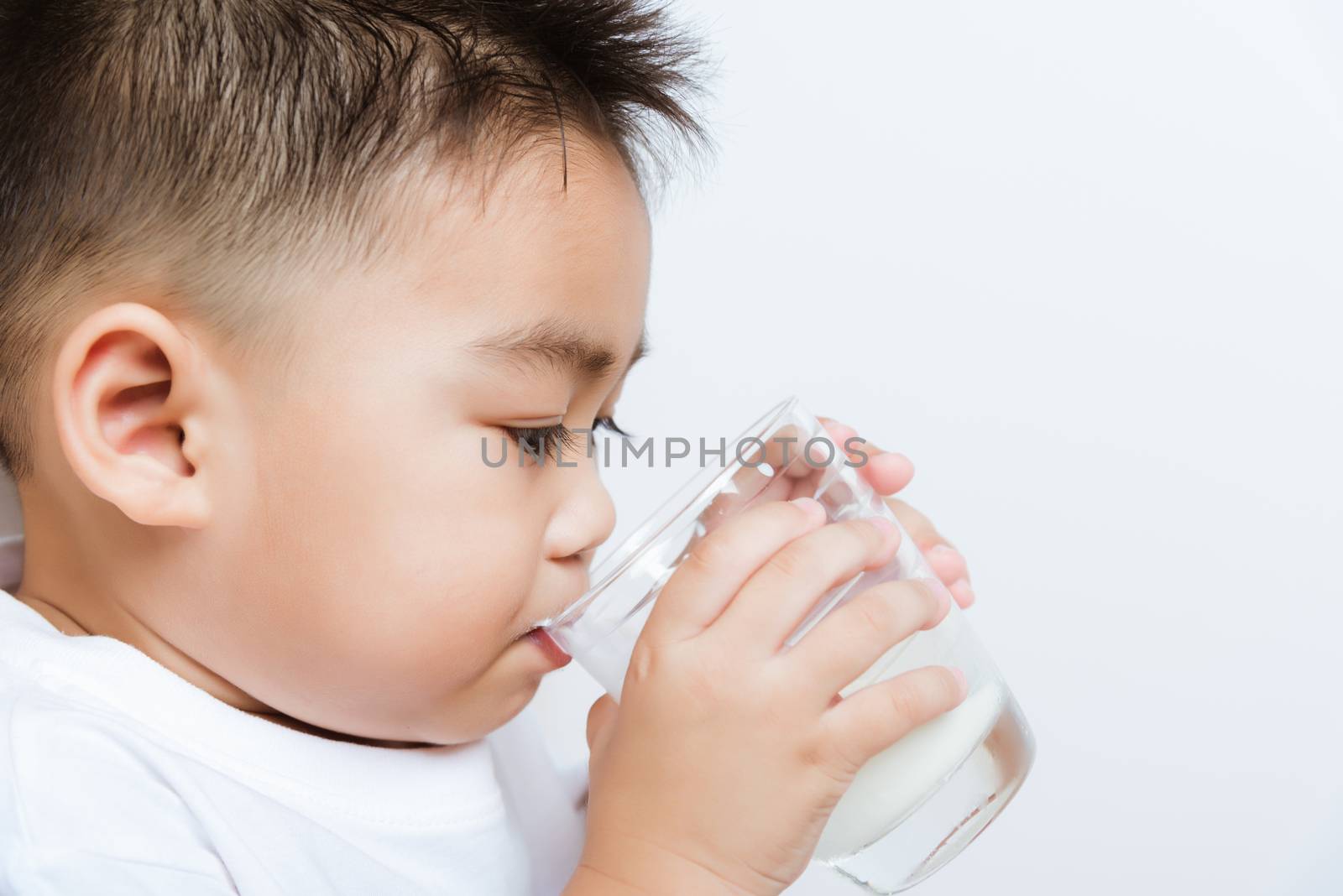 Close up of happy Asian little cute child boy hand holding milk glass he drinking white milk during sitting on the sofa at home after lunch. Daily life health care Medicine food