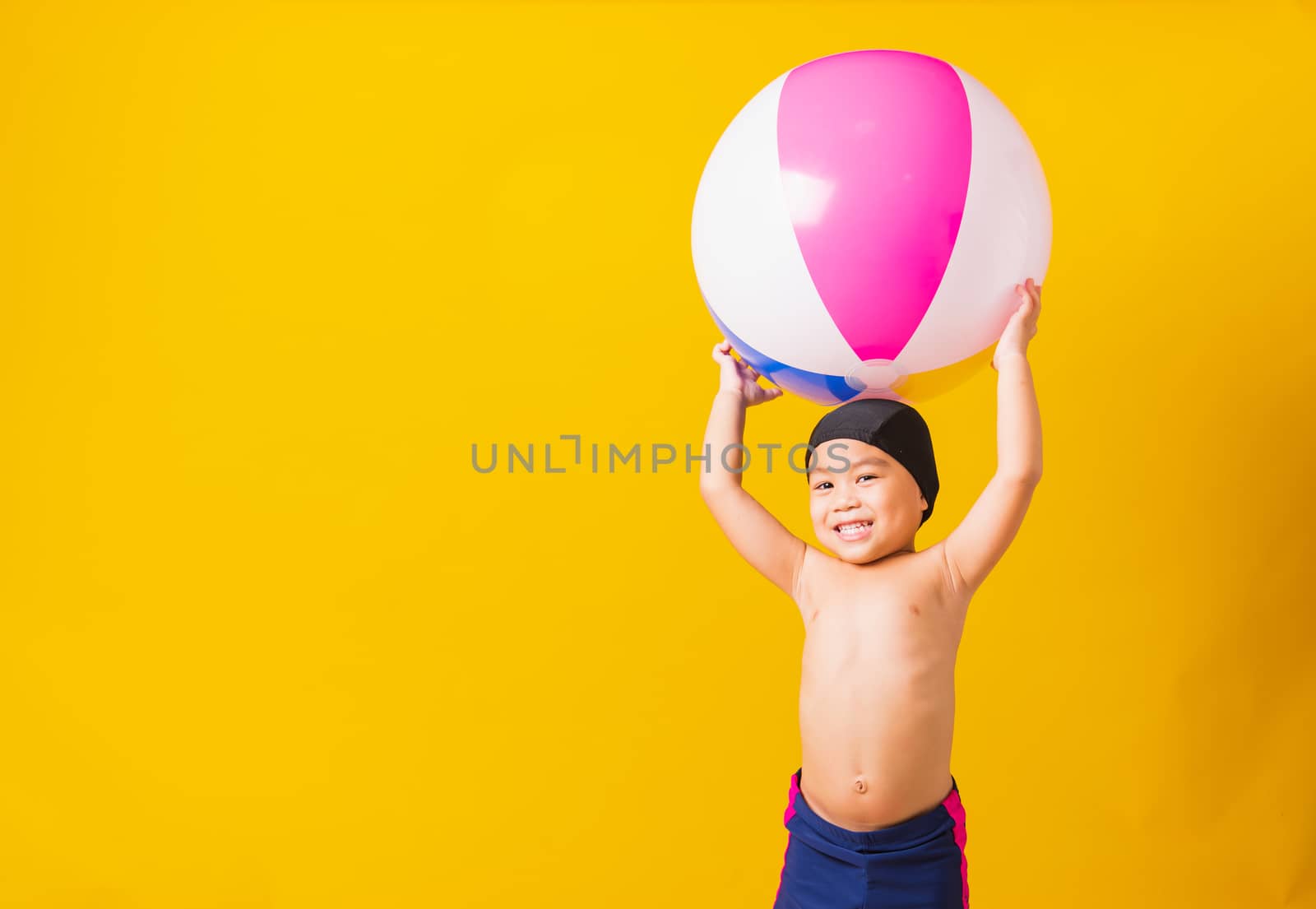 Summer vacation concept, Portrait Asian happy cute little child boy smiling in swimsuit hold beach ball, Kid having fun with inflatable ball in summer vacation, studio shot isolated yellow background