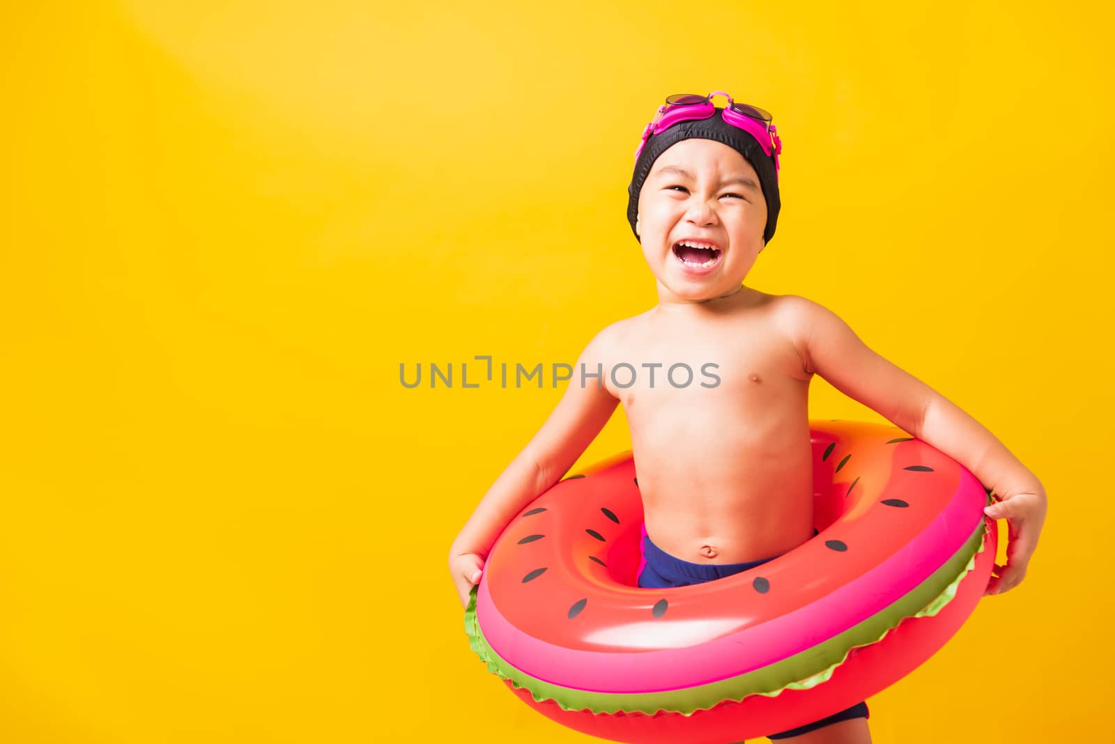 Summer vacation concept, Portrait Asian happy cute little child boy wear goggles and swimsuit hold watermelon inflatable ring, Kid having fun on summer vacation, studio shot isolated yellow background