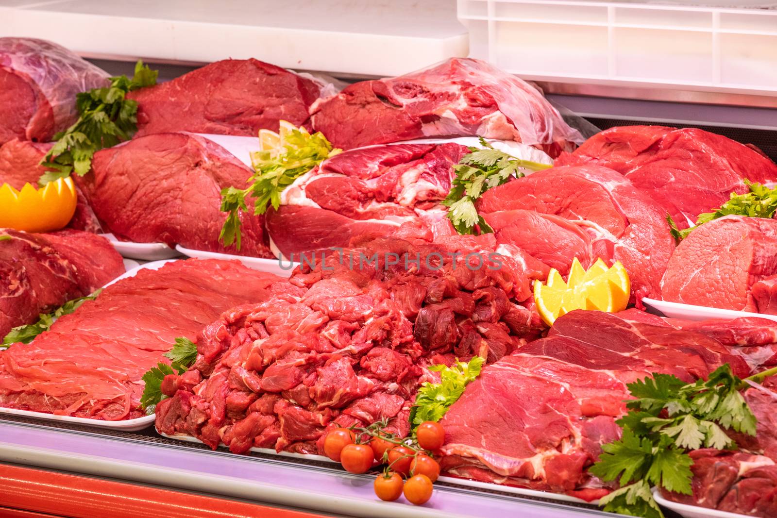 Meat department in butchery inside a mall. Various types of meat displayed in an orderly and creative way. Shelves of a food supermarket. Orange and vegetables for decoration and topping.