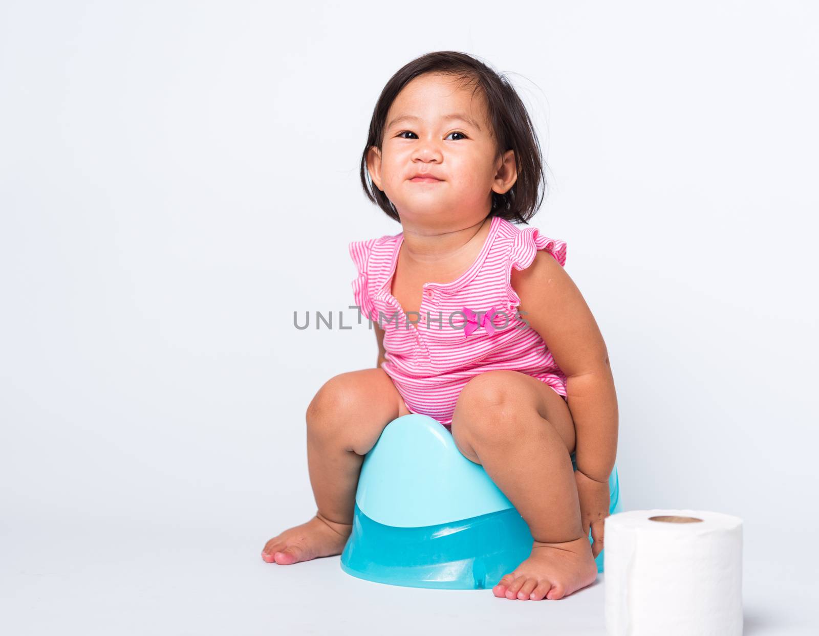 Asian little cute baby child girl education training to sitting on blue chamber pot or potty with toilet paper rolls, studio shot isolated on white background, wc toilet concept